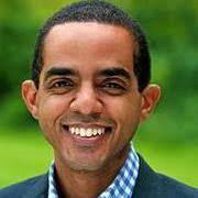 Danilo Contreras headshot with short black hair, navy blazer and blue and white checkered shirt, smiling.