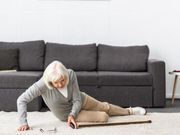 Older woman on the floor after falling with gray sofa in the background.
