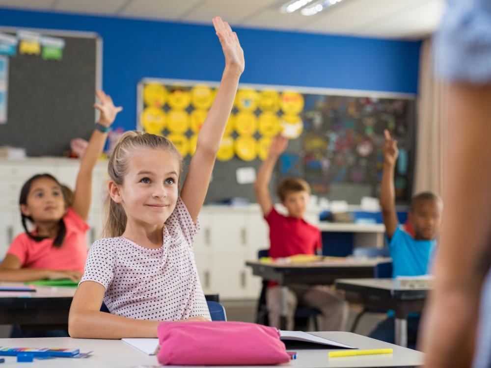 Young girl in class with her hand raised