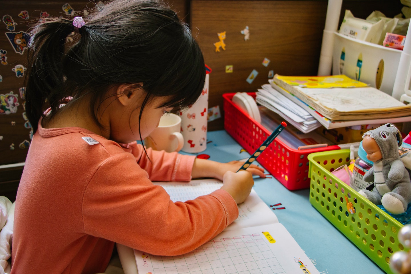 Young girl with black pony tail and orange shirt completing worksheet in school