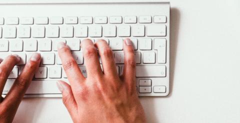 Photo of two hands typing on a keyboard.