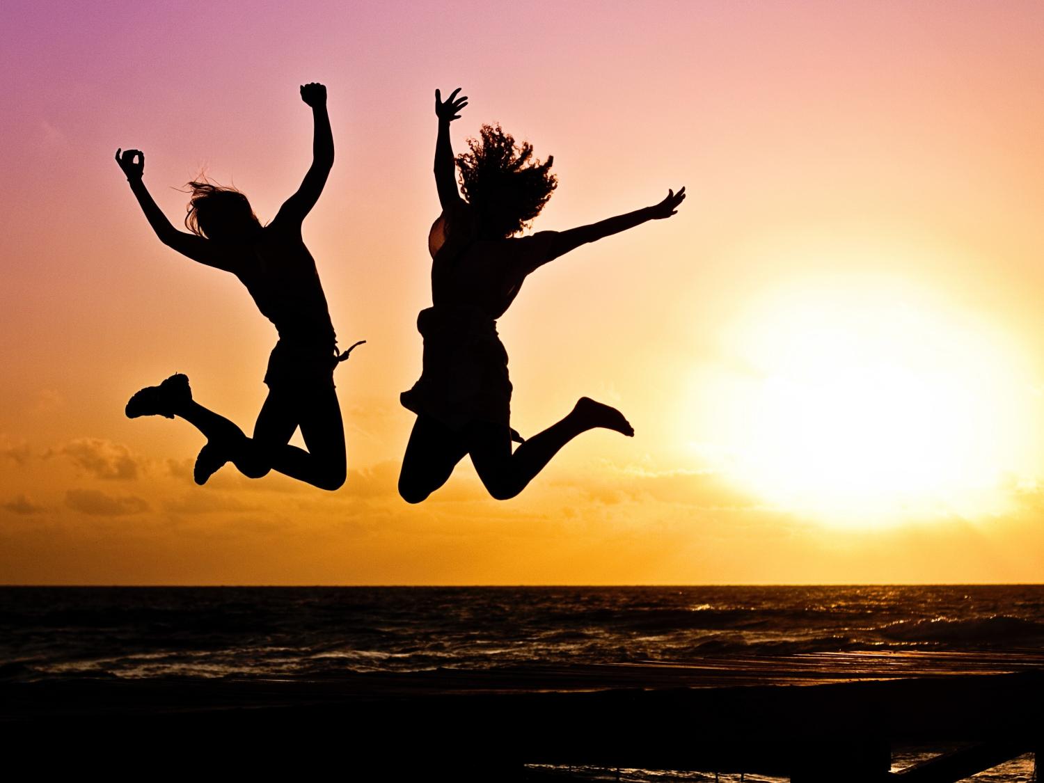 Two young girls jumping in front of sunset