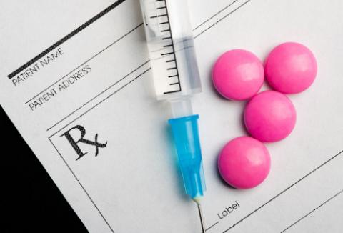 Photo of pills and a syringe on top of a prescription pad.