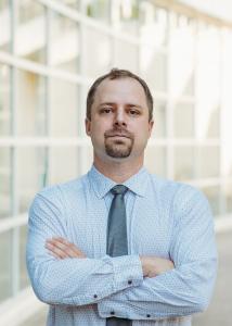 Photo of Ashton Verdery with short hair, goatee, blue shirt, tie, and arms crossed in front..