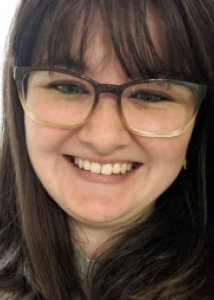 Headshot of Brittany Gay, a woman with long brown hair with bangs and glasses.