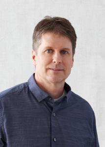 Headshot of Damon Jones, short salt and pepper hair, blue button up shirt.