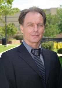 Headshot of Dusan Ramljak, a white man with dark blonde hair wearing a grey suit with grey shirt and pinstriped tie.