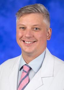 Headshot of Stephen Sandelich, a white man with grey-silver hair wearing a white lab coat, blue shirt and pink and blue tie.