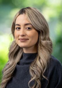 Caucasian woman with long blonde wavy hair, confident smile, brown eyes, wearing a grey cashmere sweater