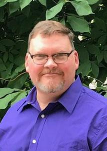 Headshot of Jeffrey Ulmer outside with short, light hair wearing a purple dress shirt and glasses. 