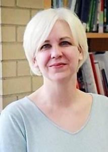 Headshot of Jenny Van Hook in front of a bookshelf with blonde hair wearing a grey shirt. 
