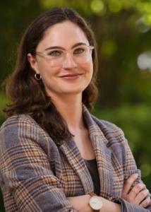 young caucasian woman with long auburn hair and green eyes, wearing glasses, small gold loop earrings and a nice classic autumn coloured plaid blazer