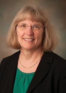 Headshot of Marianne Hillemeier with glasses and short, blonde hair wearing green shirt and black suit jacket. 