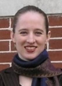 Headshot of Mary Shenk in front of a brick wall with hair pulled back wearing a scarf.