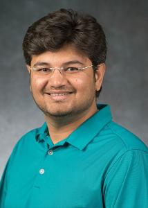 Headshot of Arpan Yagnik, a man with short, fluffy dark hair and glasses wearing a teal colored collared shirt.