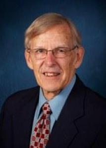 Headshot of Gordon with short gray hair, glasses, light blue shirt, red patterned tie, and dark jacket.