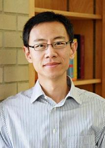 Headshot of Guangqing Chi with short black hair, black rimmed glasses, wearing a blue and white striped shirt.