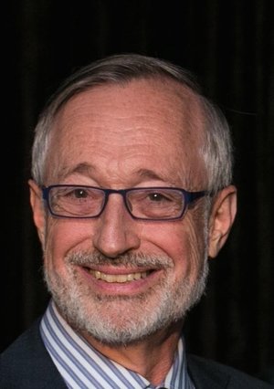 Headshot of Paul with gray hair, beard, glasses, blue and white striped shirt, and dark gray jacket.