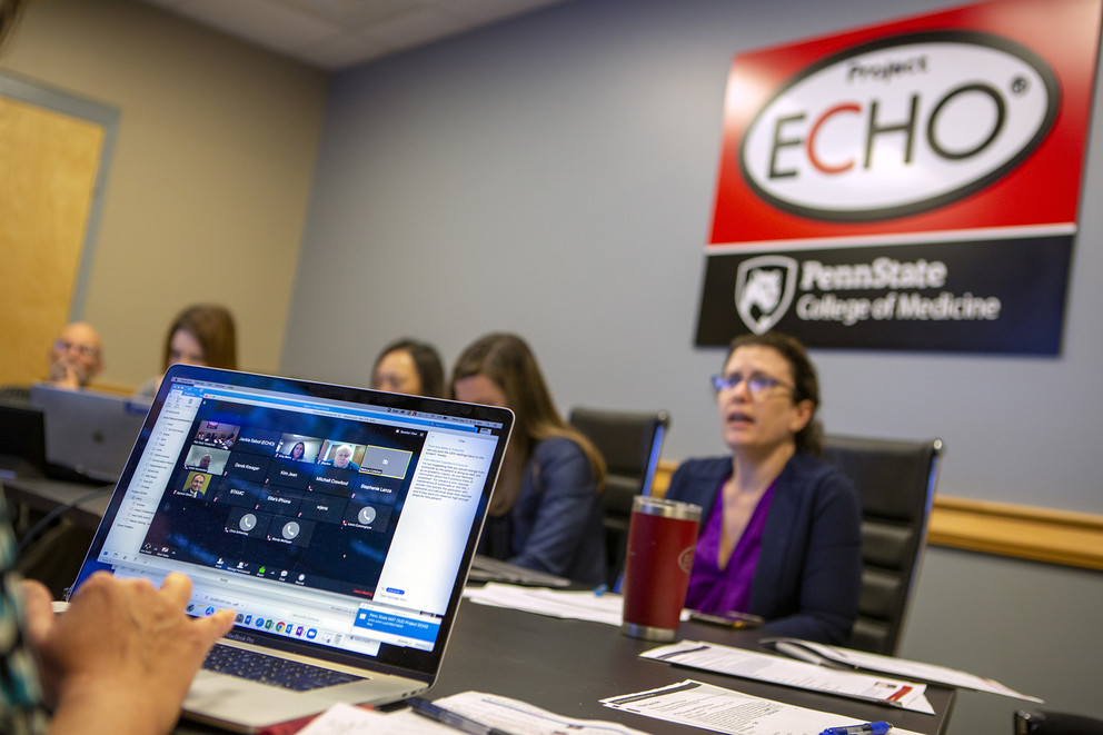 Photo of people around a conference table and a laptop screen open to a video conference with a logo for Project ECHO at Penn State College of Medicine on the wall in the background.