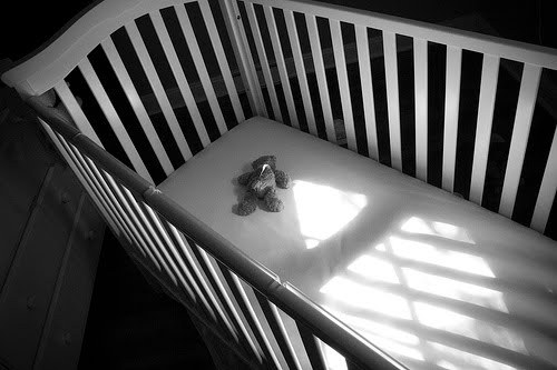Photo of a crib with a lonely teddy bear, but no baby.