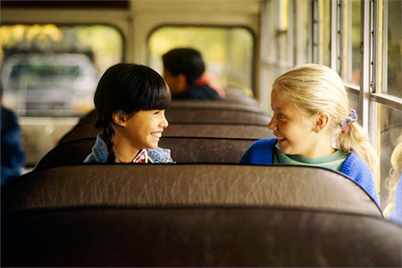 Two children talking on a school bus.