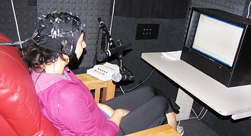 Photo of a woman sitting in a chair with a device on her head while looking at a screen.