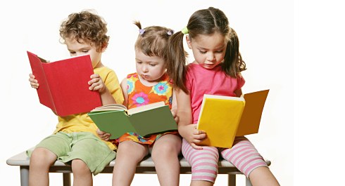 Photo of three children sitting on a bench and reading books.