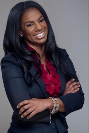 Young African American woman with beautiful long black wavy hair, brown eyes, friendly smile, wearing a navy blue suit and nice floral blouse with red flowers; arms crossed in a confident and friendly way