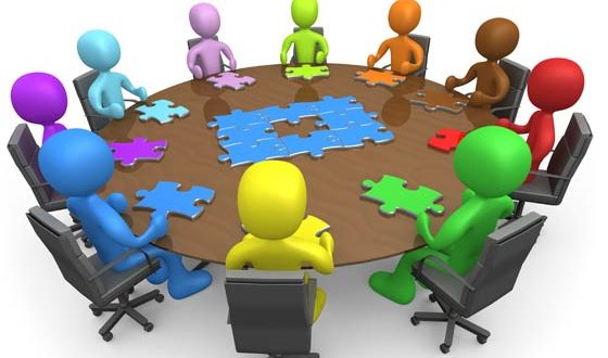 Graphic of multi-colored people sitting in office chairs around a table putting together pieces of a puzzle.