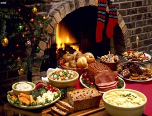 Photo of various holiday foods on a table, a decorated tree, and socks hanging in front of a fireplace.