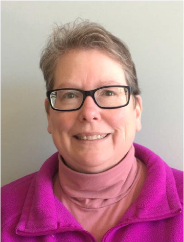 Headshot of Kathleen with short brown hair, glasses, pink top, and purple jacket.