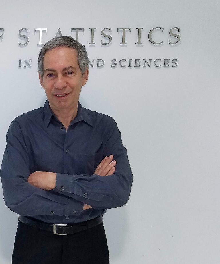 Photo of Michael Sobel with gray hair, dark gray shirt, black belt and pants, standing in front of a sign for the Department of Statistics.