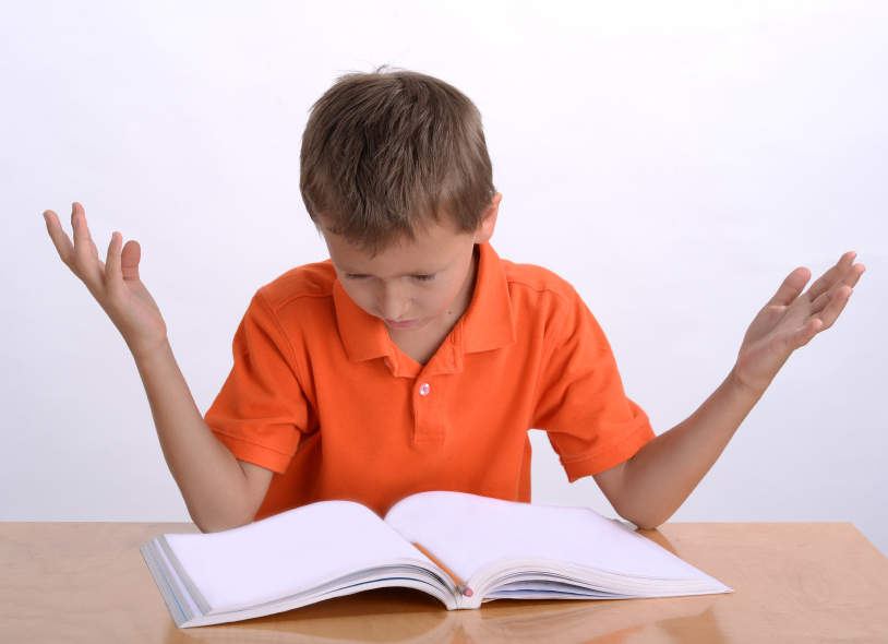 Photo of a child sitting in front of a workbook, looking frustrated.