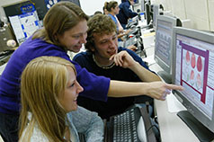 Photo of three students gathered around a computer screen.