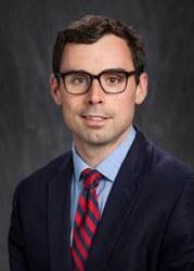 Headshot of Brian Theide with black hair, glasses, blue shirt, red and blue striped tie, and dark blue jacket.
