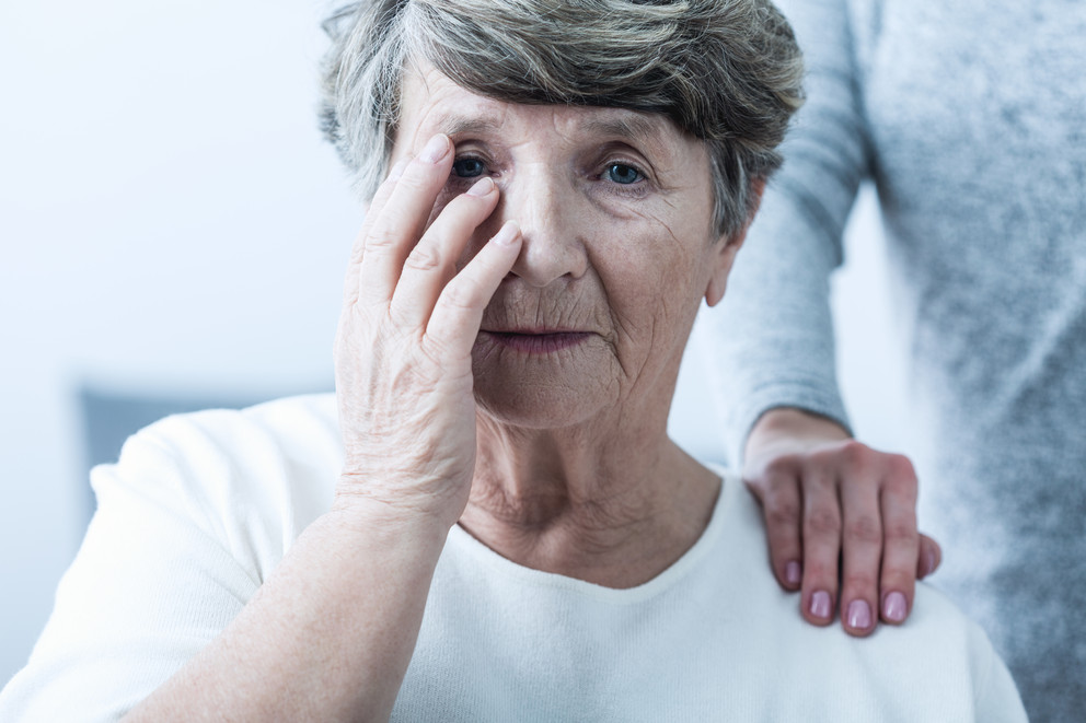 Photo of a distressed older woman with a younger hand on her shoulder.