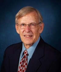 Headshot of De Jong with gray hair, glasses, blue shirt, tie with red squares, and navy jacket.