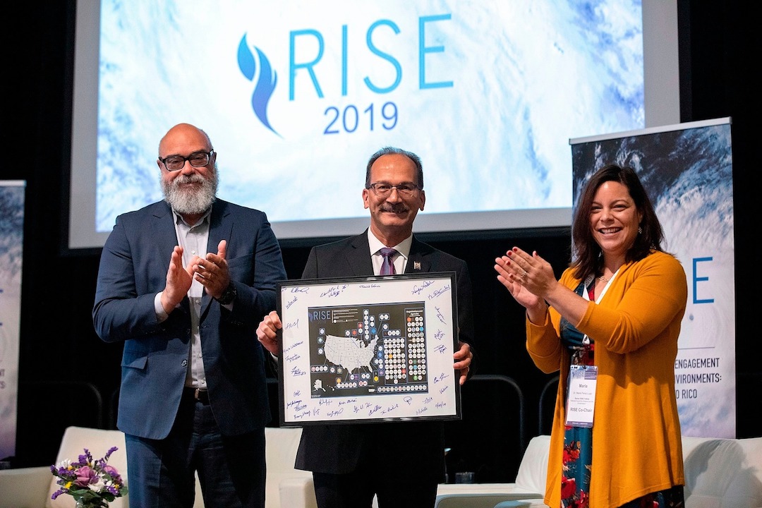 Cecilio Ortiz-Garcia, left, and Marla Perez-Lugo, right, present Havidán Rodríguez, president of the University at Albany, State University of New York, with a map depicting the reach of the RISE Network.