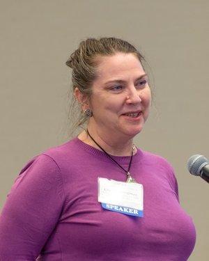 Photo of Claudia Brugman with her hair pulled back and wearing a purple blouse.