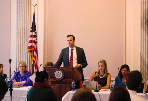 Max Crowley speaking at a podium with panelists on either side.