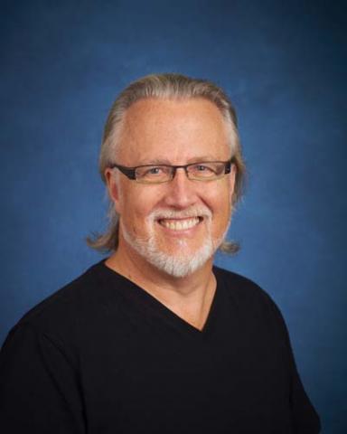 Headshot of David Baker with long gray hair, glasses, beard, and black shirt.