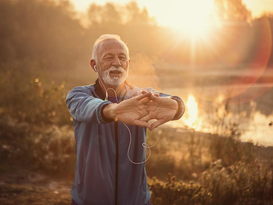 Older man with headphones doing yoga outside at sunrise.