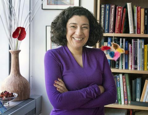 Headshot of Koraly Pérez-Edgar with black hair and purple blouse, standing next to a decorative vase and a bookshelf.