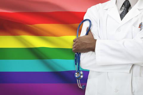 A doctor standing in front of a rainbow flag.