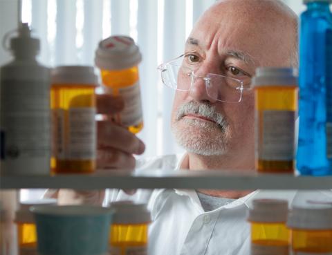 A man with gray hair and glasses looking through the prescriptions in his medicine cabinet.