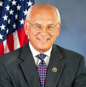 Headshot of Paul Tonko with white hair, glasses, white shirt, blue checkered tie, gray jacket, and the United States flag behind him.