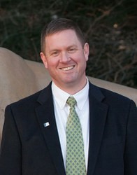 Daniel Perkins headshot in black suit and green tie.