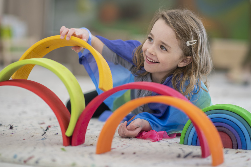 Preschool girl playinig in sandbox with colored rings.