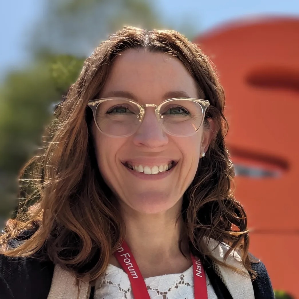 Anne Pisor with long, dark curly hair, glasses, smiling.