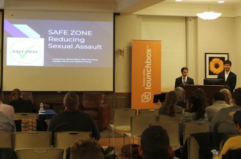 Photo of a presentation with a Lauchbox banner by the podium and "Safe Zone: Reducing Sexual Assault" on the projector screen. 